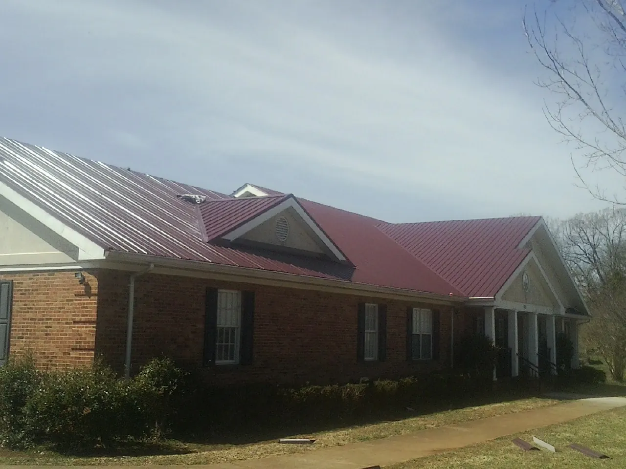 Red metal roof with gabled entries on a long brick building, from a Hail Damage Roof Repair job in Waldron