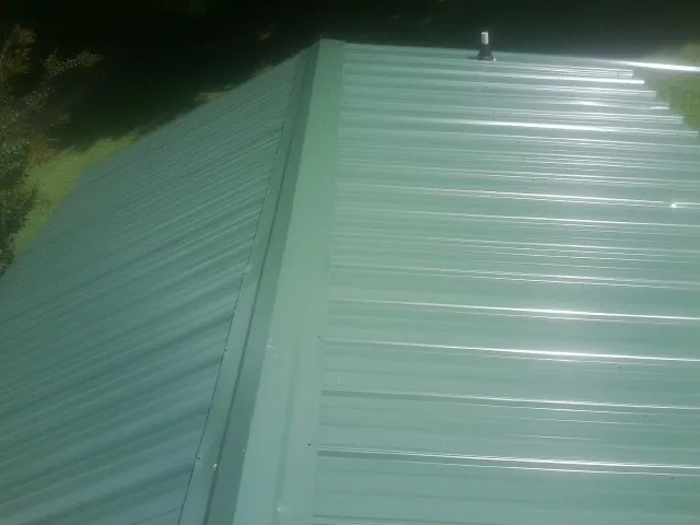 New green metal panels meeting at the ridge of a roof — Flat Roof Repair work by our crew in Waldron