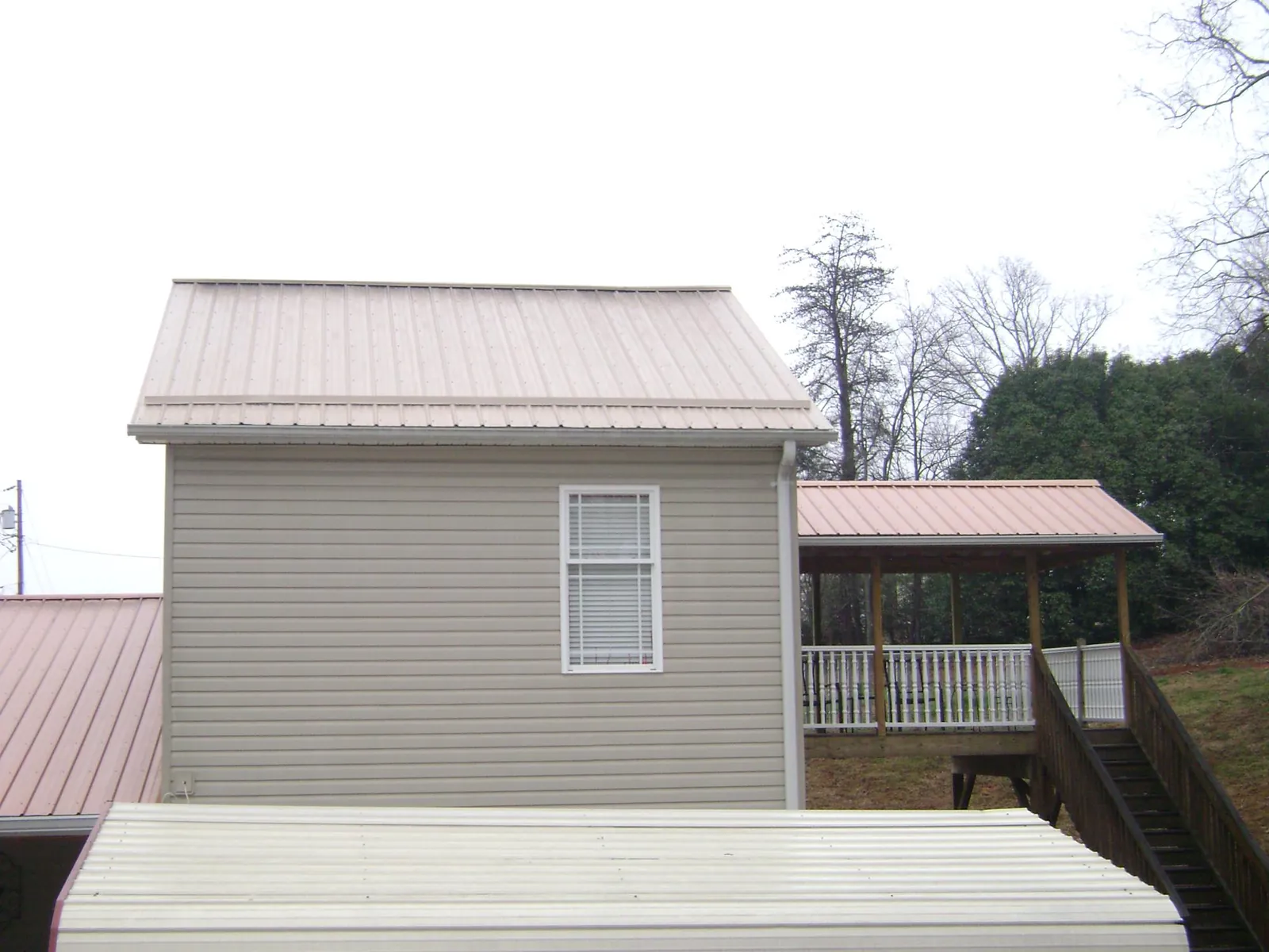 Tan metal roofs on a two story addition and attached porch, from a Roof Replacement job in Waldron